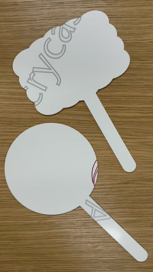 Two white laser cut acrylic signs with handles, one rectangular scalloped shaped and one circle shaped sign, placed on a wooden surface. Both signs have their protective film removed in the video to show the white acrylic. 