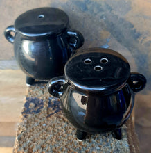 Load image into Gallery viewer, Two black ceramic cauldron-shaped salt &amp; pepper shakers placed on a wooden surface.
