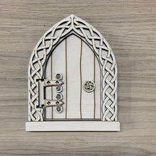 Load image into Gallery viewer, A wooden laser cut Celtic Fairy Door with intricate knotwork design and a functioning hinged door. Item displayed on a wooden background.

