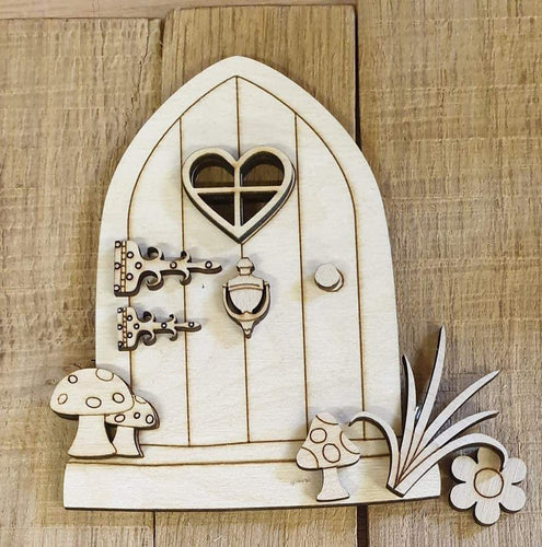 A laser cut fairy door with a layered door knocker, handle, hinges, window, mushrooms, grass, and flowers.
