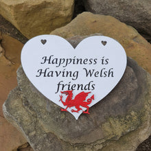 Load image into Gallery viewer, A heart shaped laser cut plaque, painted white with a layered Welsh dragon shape. The dragon shape is painted red and attached on top of the heart. The plaque is placed on top of large stones for a background.
